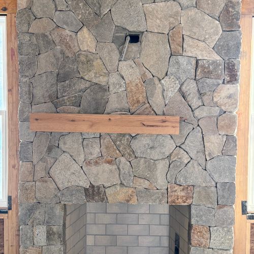 Stone fireplace with irregular gray rocks and wooden mantel shelf