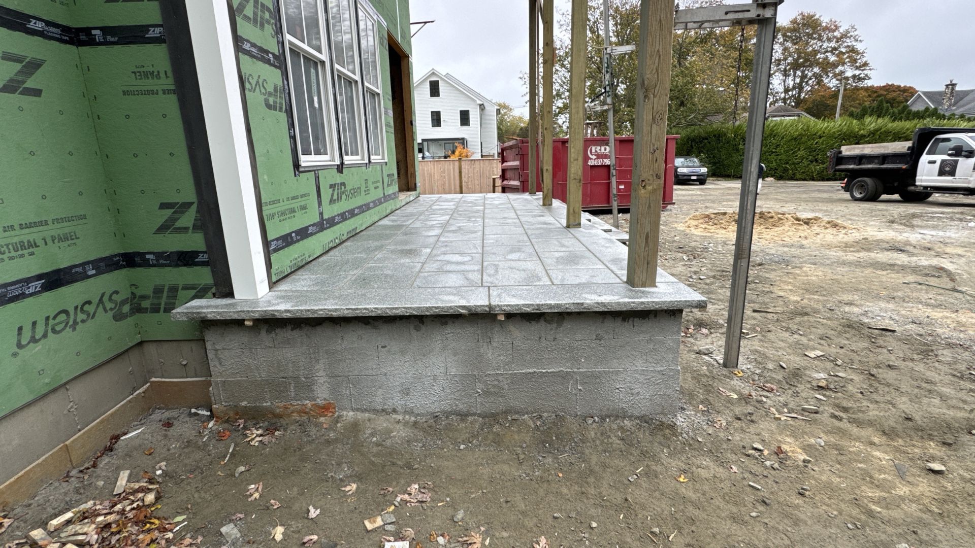 Construction site with concrete porch, green siding, and red dumpster in background
