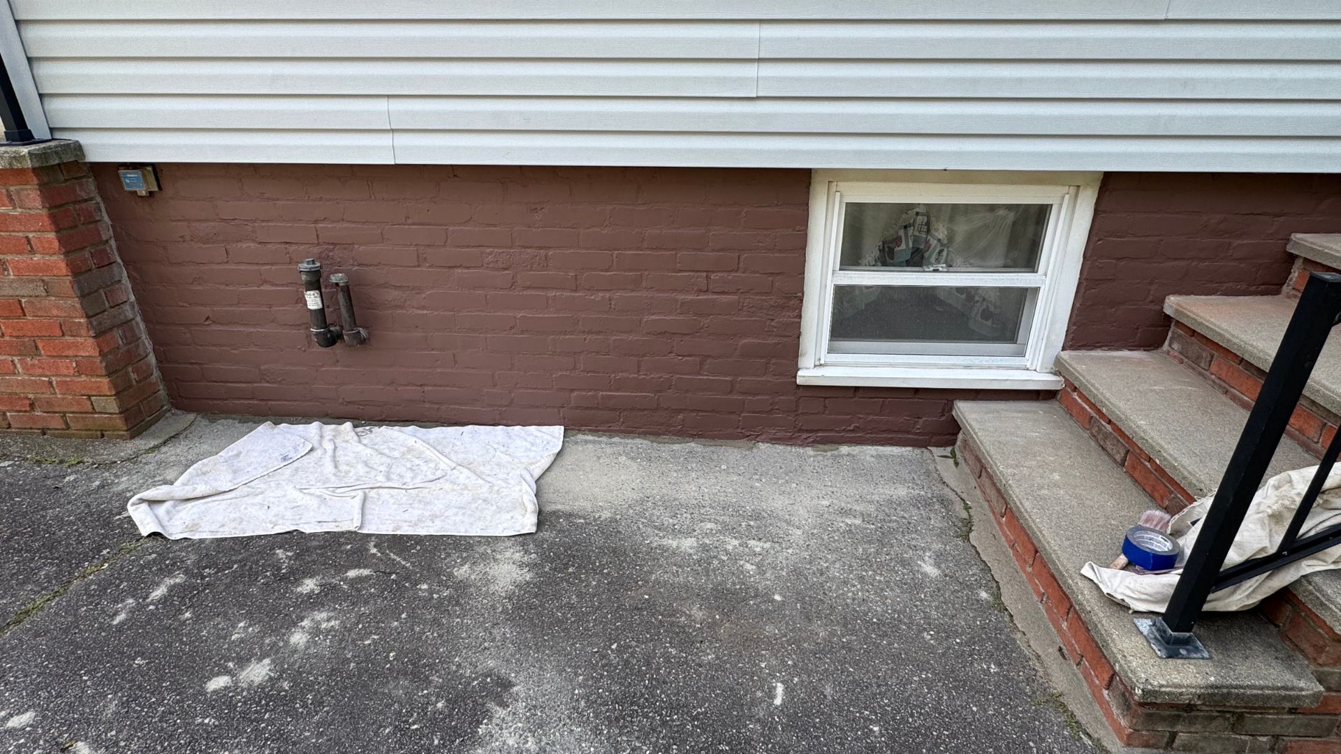 White sheet on concrete beside brick wall with window and exterior pipes